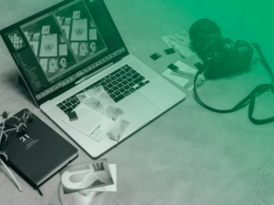 Mesa de trabalho com notebook exibindo edição de imagens, câmera fotográfica, cartões de memória e material gráfico, sob efeito degradê verde.