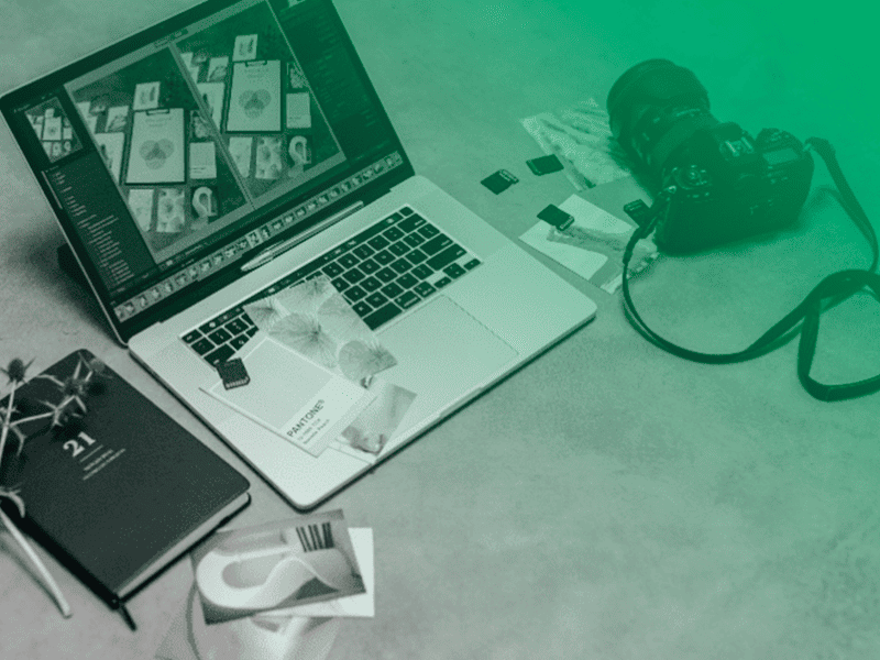 ferramentas-para-investigações Mesa de trabalho com notebook exibindo edição de imagens, câmera fotográfica, cartões de memória e material gráfico, sob efeito degradê verde.